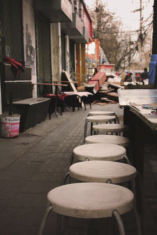 Nearby, a restaurant under demolition brings its tables out onto the sidewalk, where customers will done under the stars as the night falls